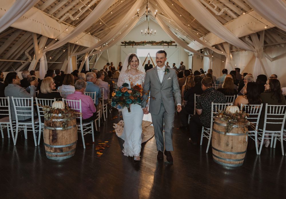 Wedding party dancing and celebrating in a rustic barn venue with exposed wooden beams and string lights.