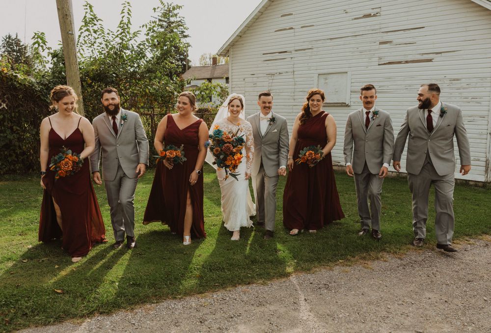 Wedding group walking and laughing together along path by rustic white barn.