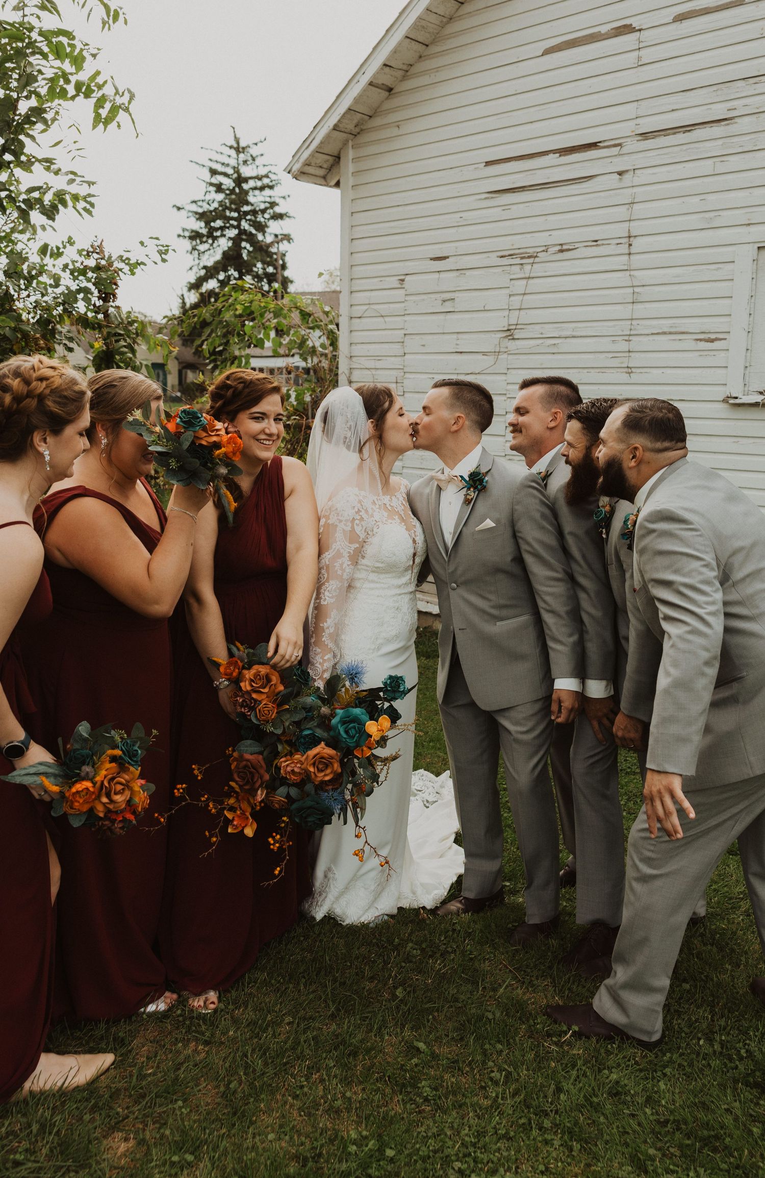 Bridal party shares laughs during informal photo session by white farmhouse.