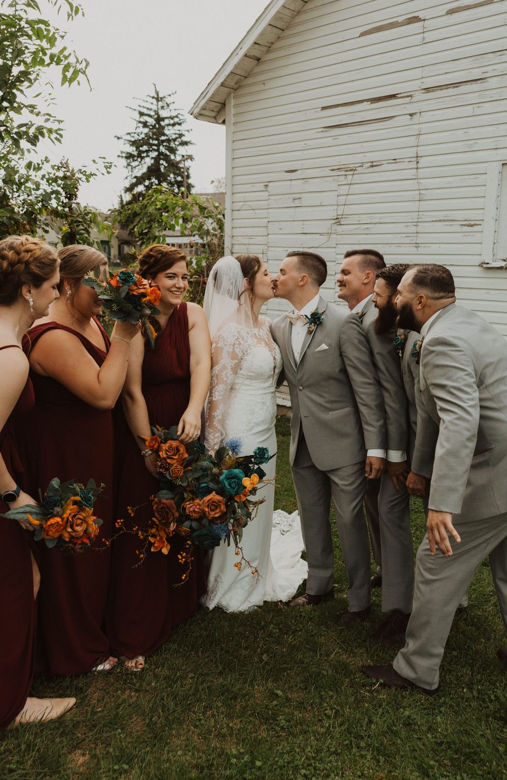 Bridal party shares laughs during informal photo session by white farmhouse.
