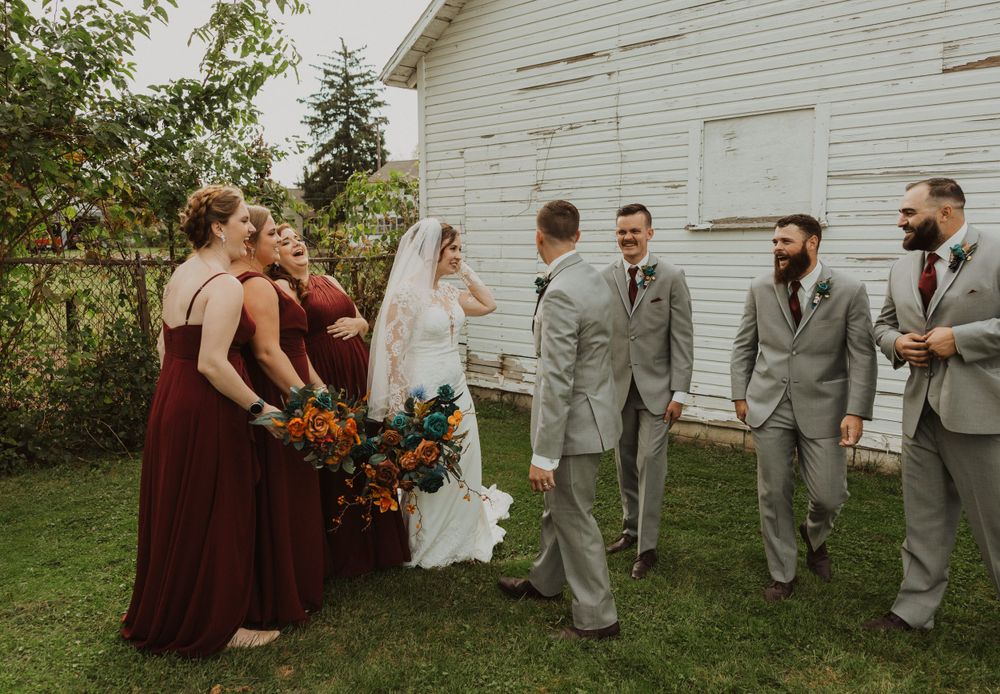 Candid wedding party photo showing natural interactions against rustic barn backdrop.