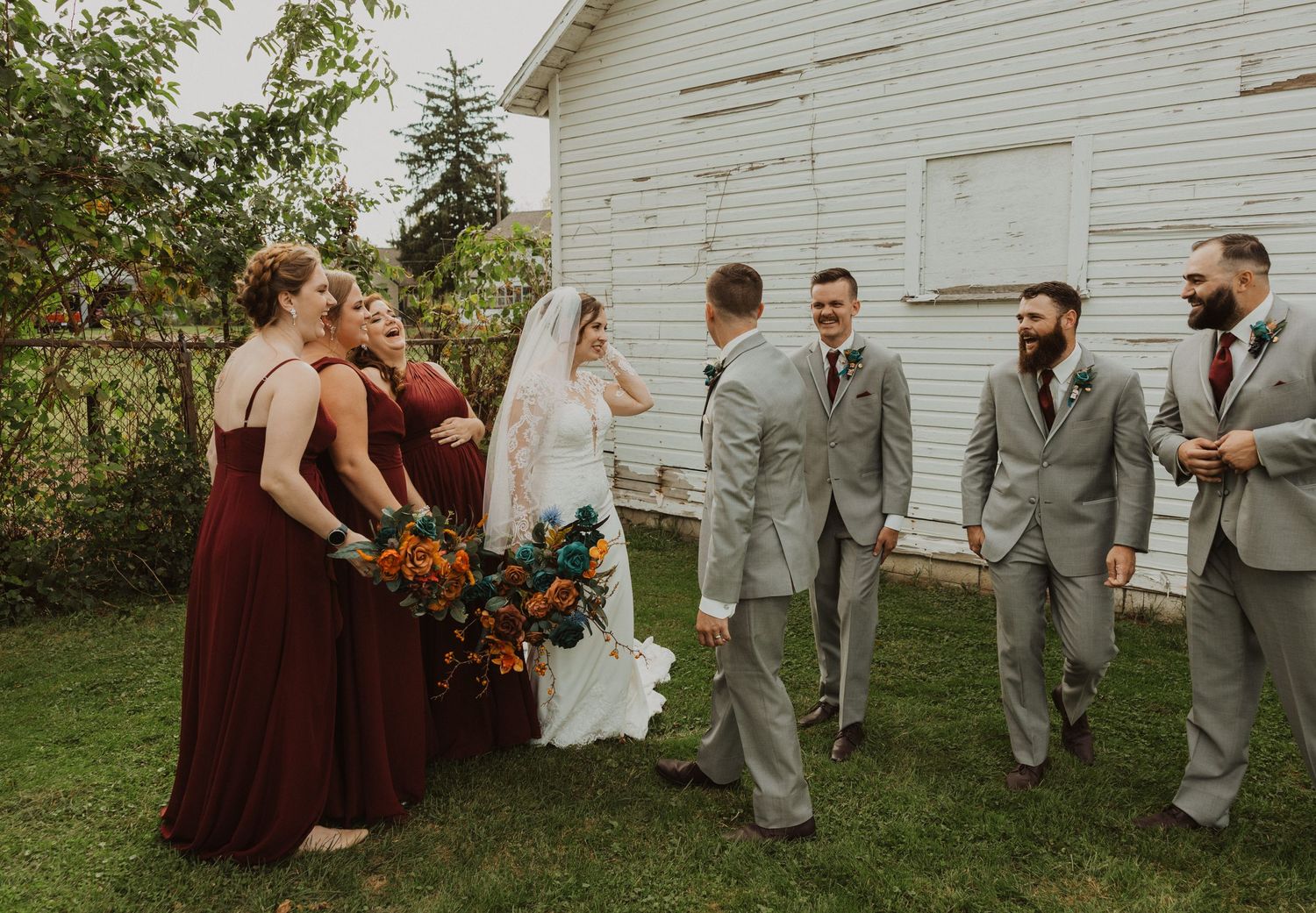 Candid wedding party photo showing natural interactions against rustic barn backdrop.