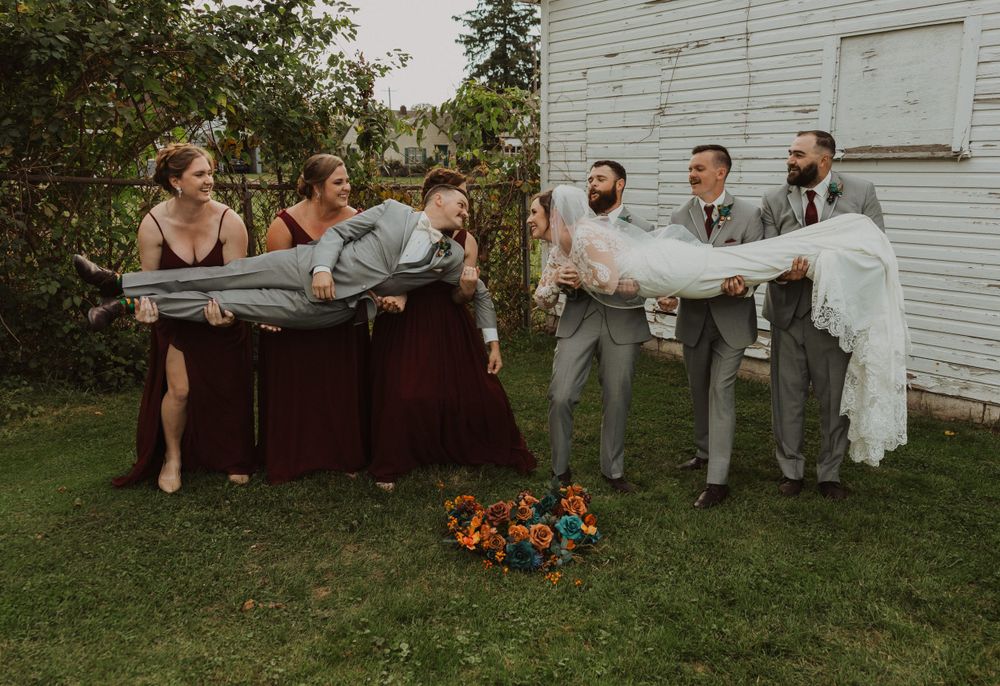 Fun wedding party photo session with creative poses against white building exterior.
