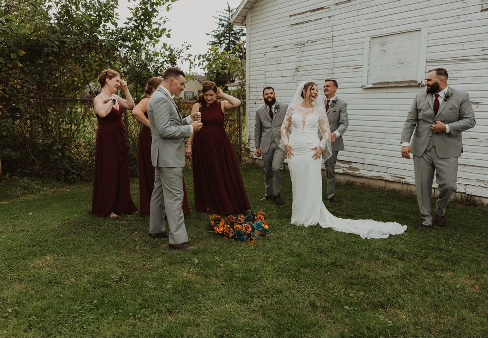 Playful wedding party poses in sequence against white barn backdrop.