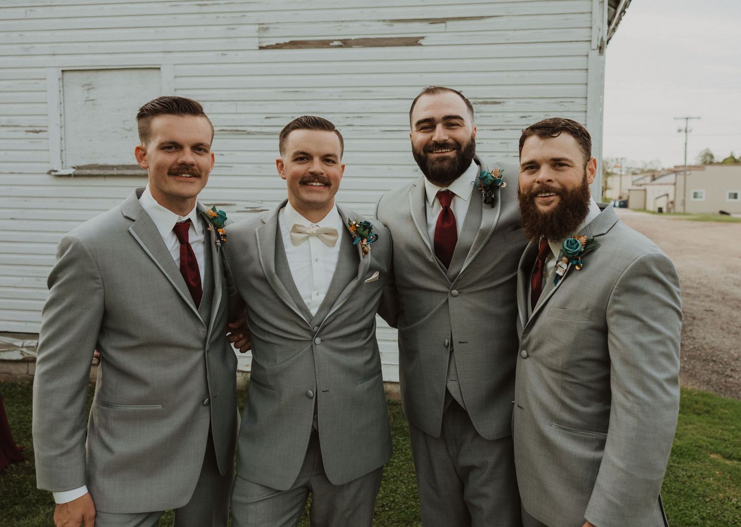 Groomsmen in matching gray suits pose together against white barn background.