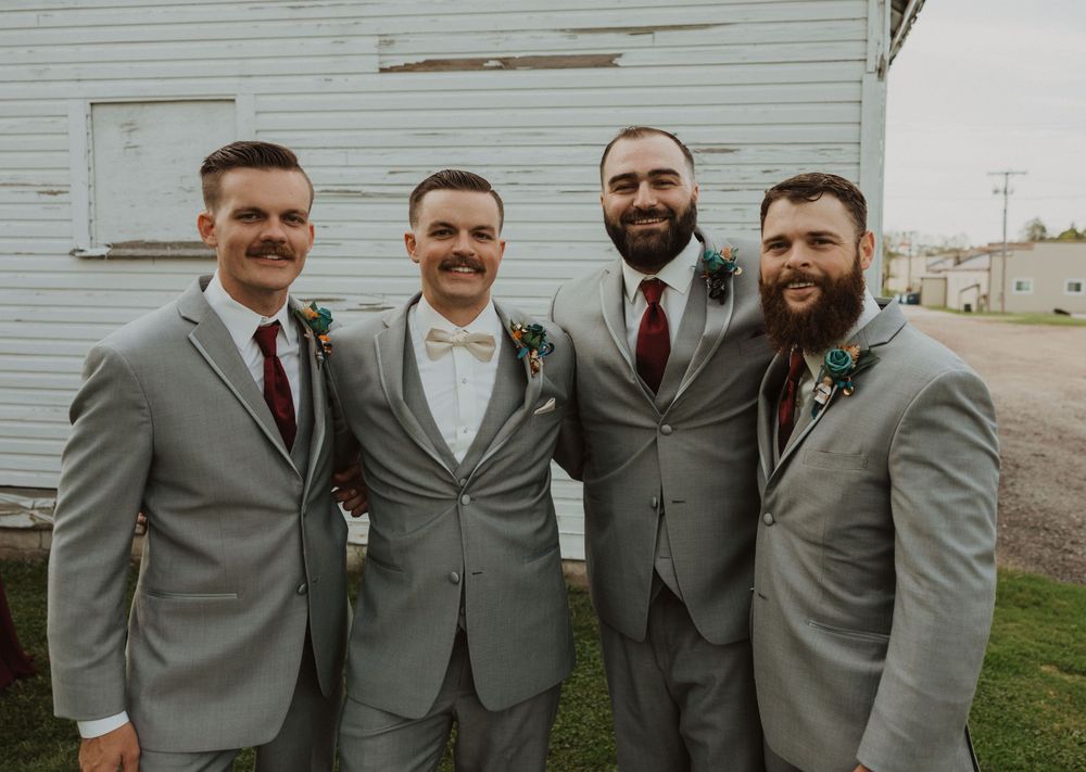 Groomsmen in matching gray suits pose together against white barn background.