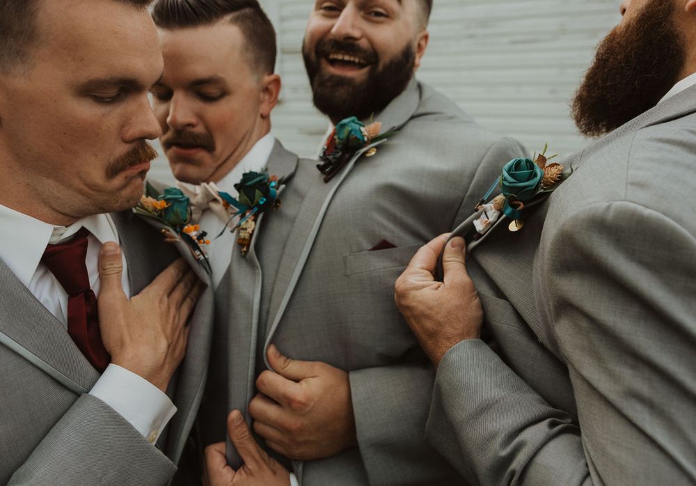 Wedding party members in gray suits share a lighthearted moment together.