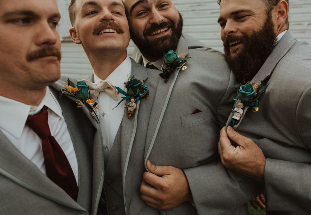 Groomsmen in gray suits laugh and joke during outdoor wedding photos.