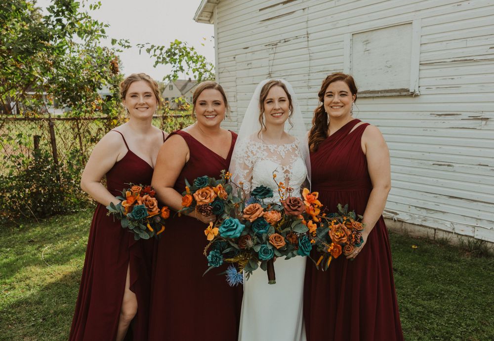 Wedding party with burgundy bridesmaid dresses gather for outdoor photos.