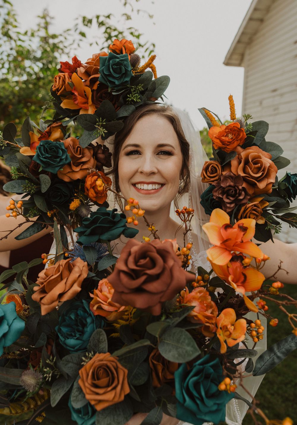 Close-up of orange and teal wedding bouquets with roses and greenery against natural background.
