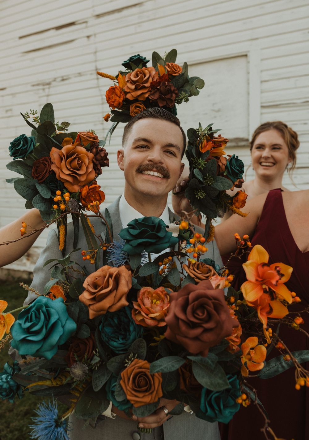Close up of vibrant orange and teal floral wedding bouquets with greenery.