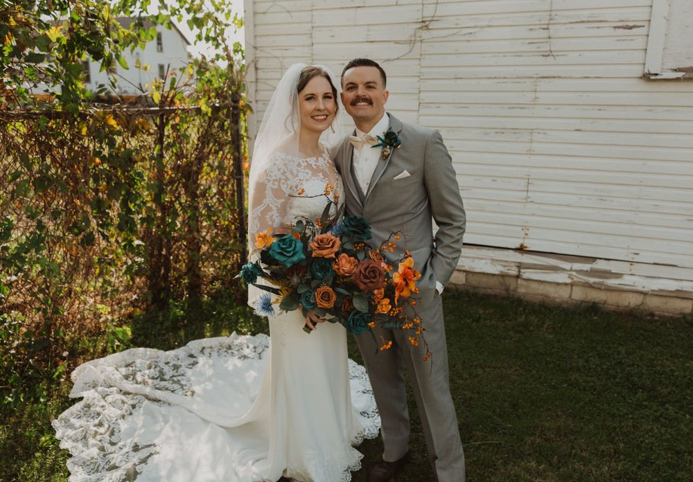 Newlyweds stand together holding vibrant fall bouquets by rustic barn.