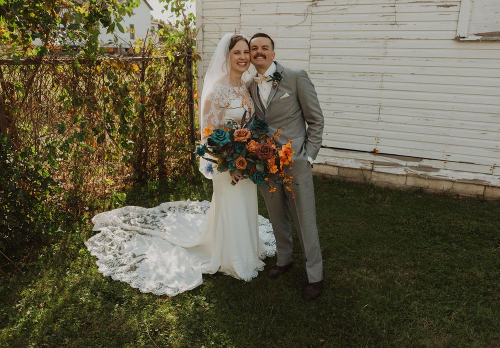Wedding couple poses outdoors with orange and teal floral arrangements.
