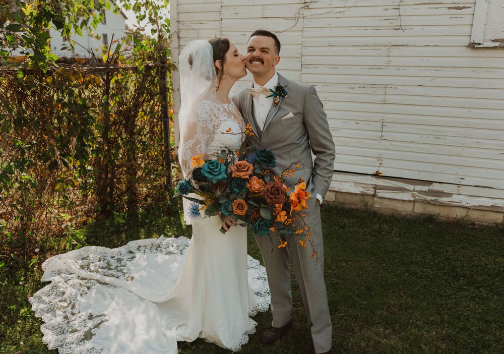 Romantic wedding portraits showcase elegant lace dress and gray suit against rustic white barn backdrop.