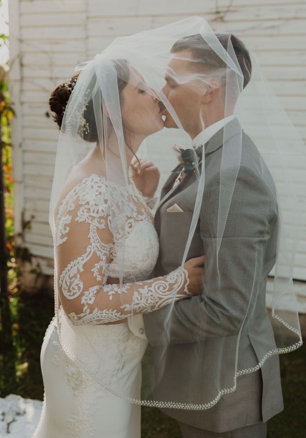 Intimate wedding moment under delicate veil with intricate lace dress details.