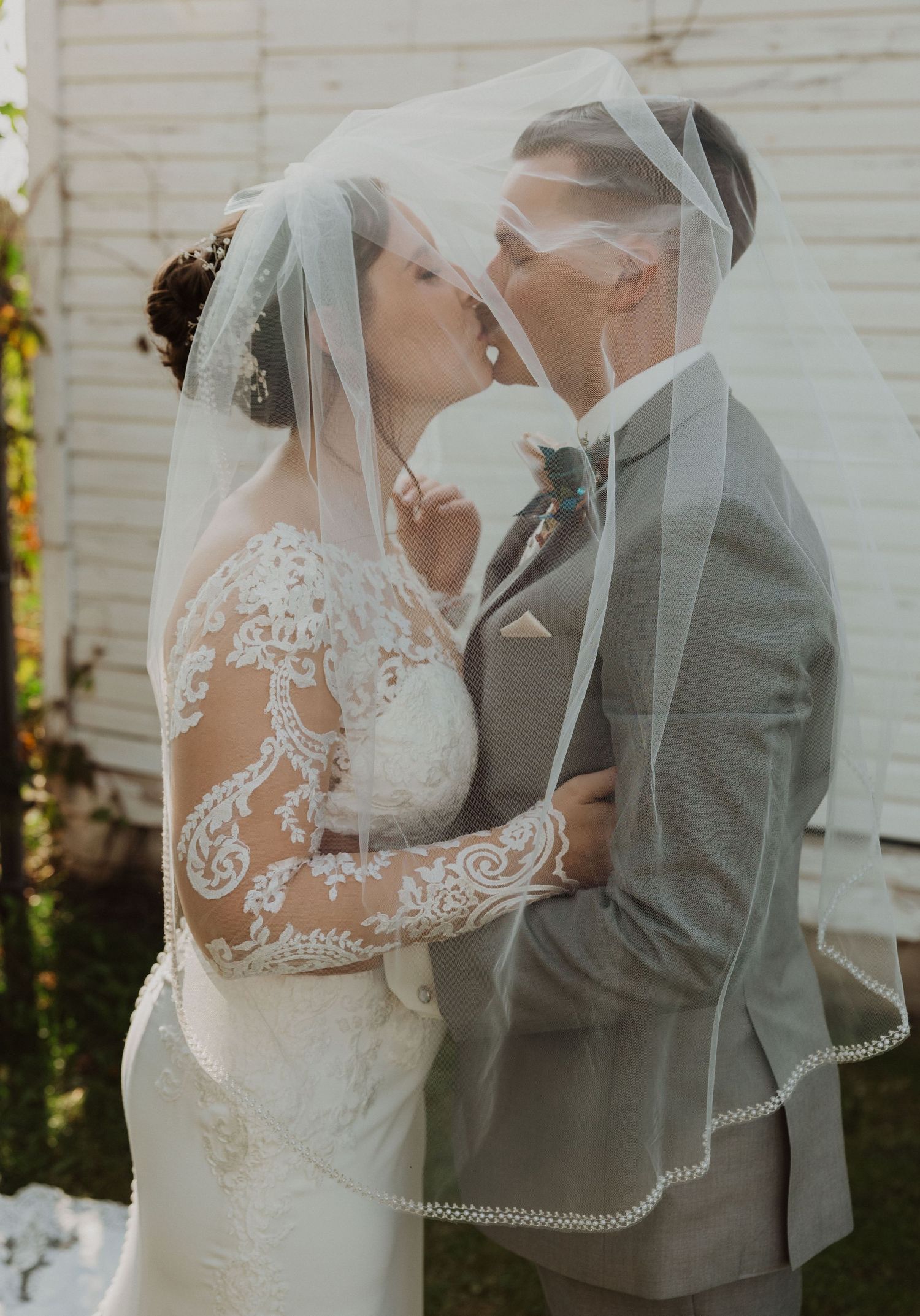 Intimate wedding moment under delicate veil with intricate lace dress details.
