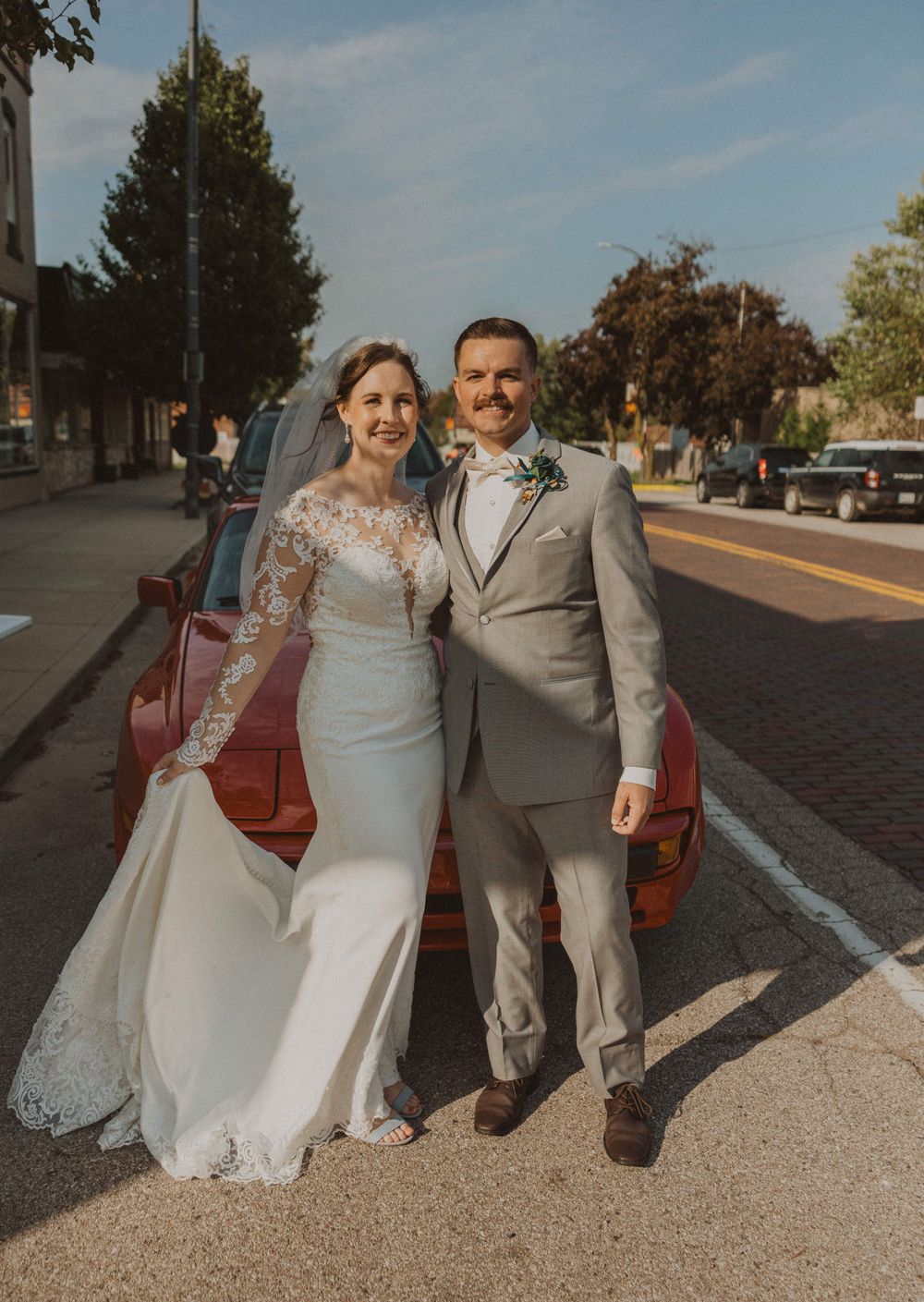 Wedding couple poses on brick sidewalk under blue autumn sky.