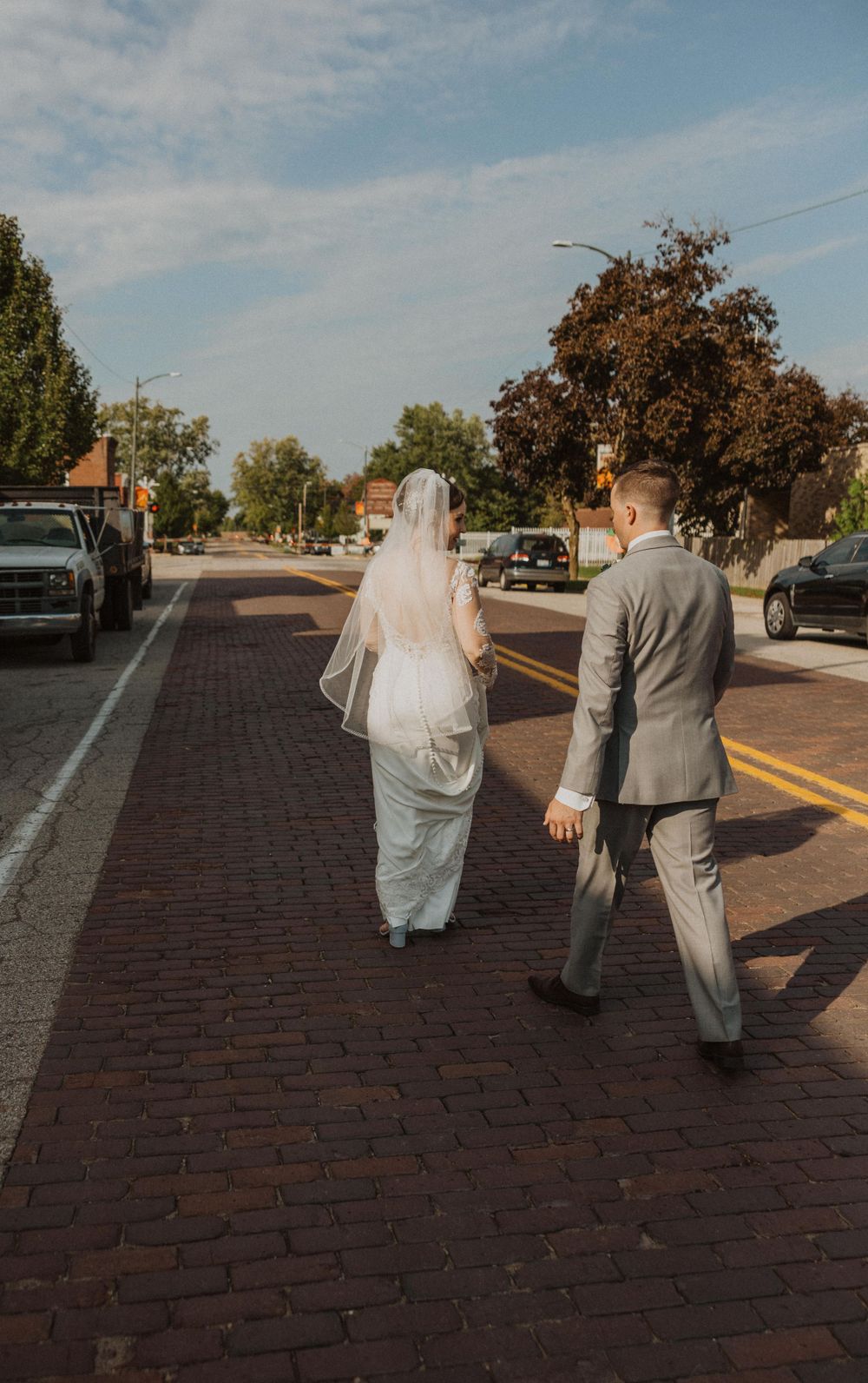 Wedding couple walks away on red brick path during sunset photoshoot.