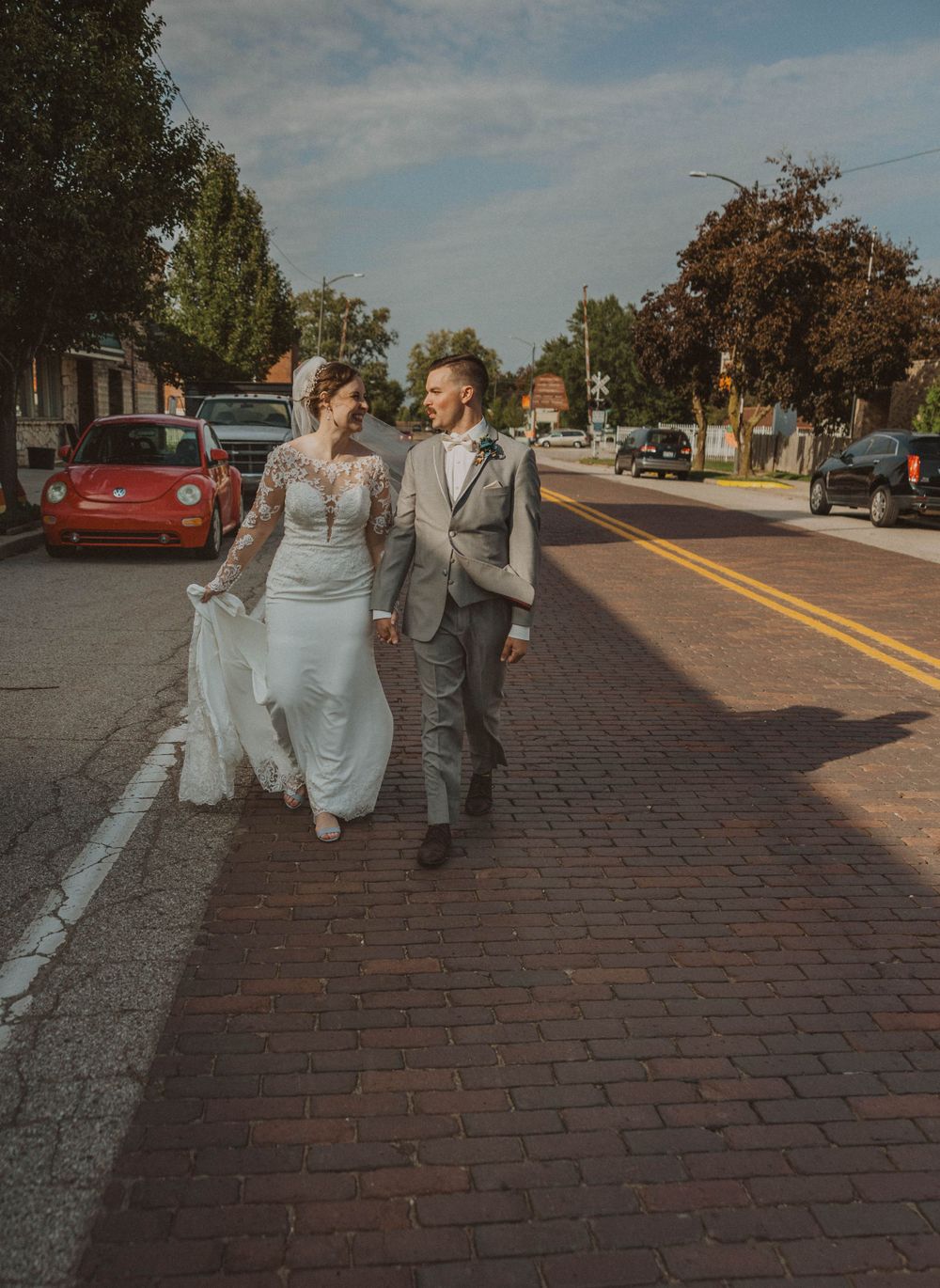 Wedding couple walks playfully along a brick-lined street with vintage buildings in the background.