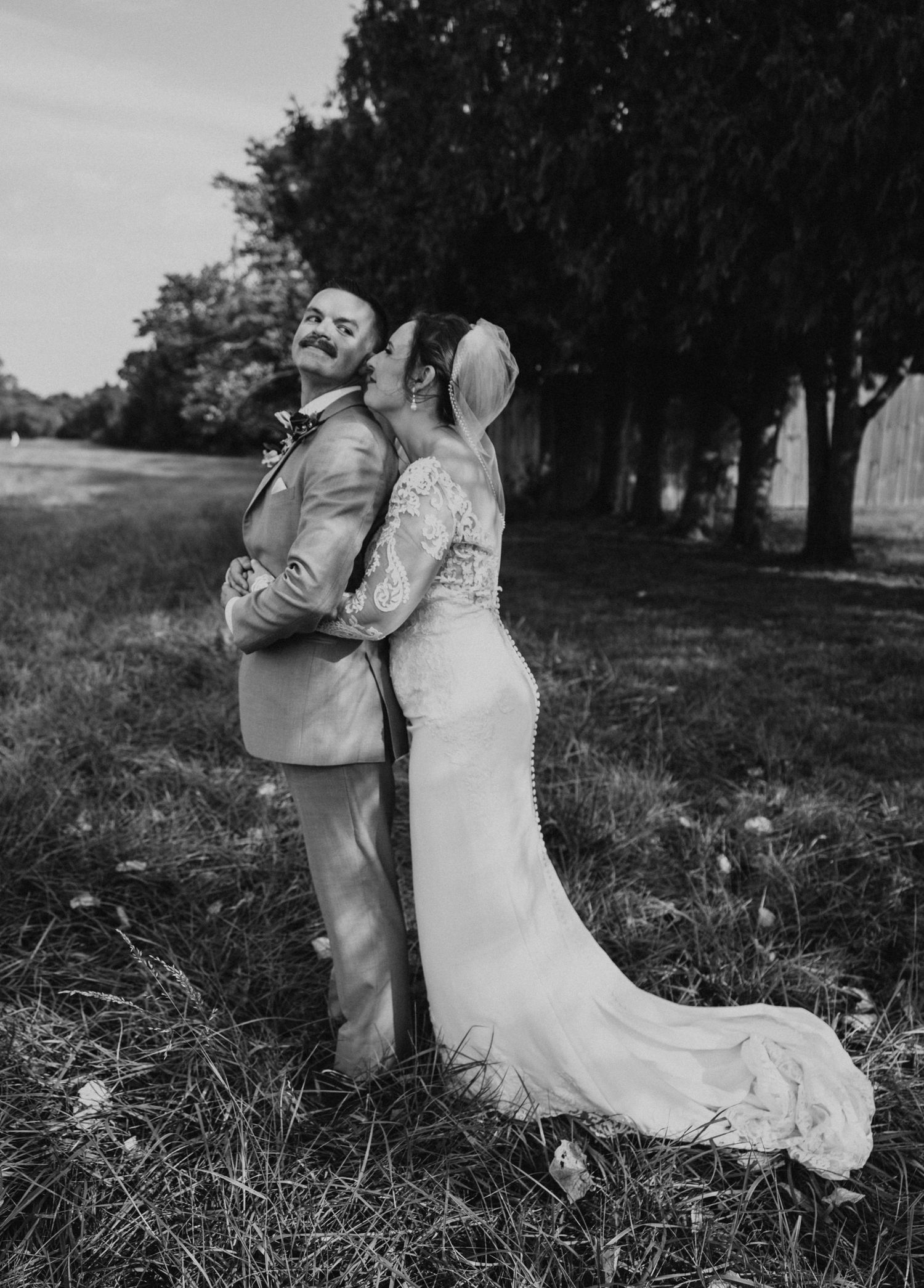 Black and white wedding portrait of couple in field with flowing dress and natural elements.