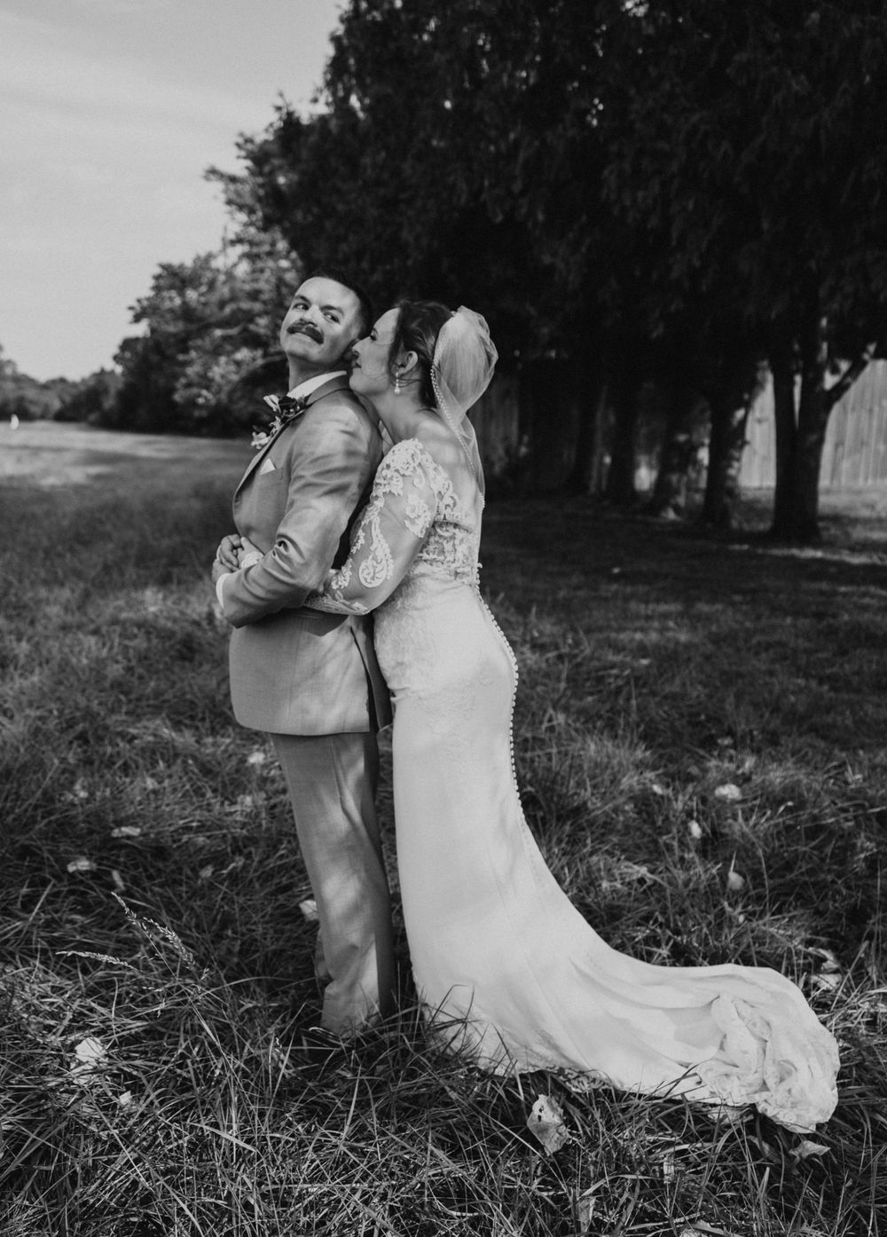 Black and white wedding portrait of couple in field with flowing dress and natural elements.