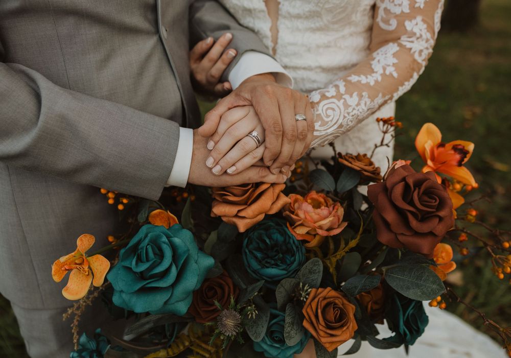 Elegant floral arrangement featuring orange and teal roses with complementary greenery and foliage.
