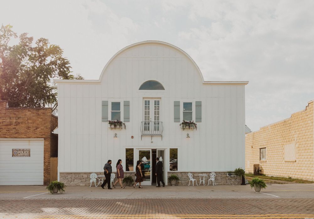 White modern wedding venue exterior with arched architecture and brick paved courtyard.