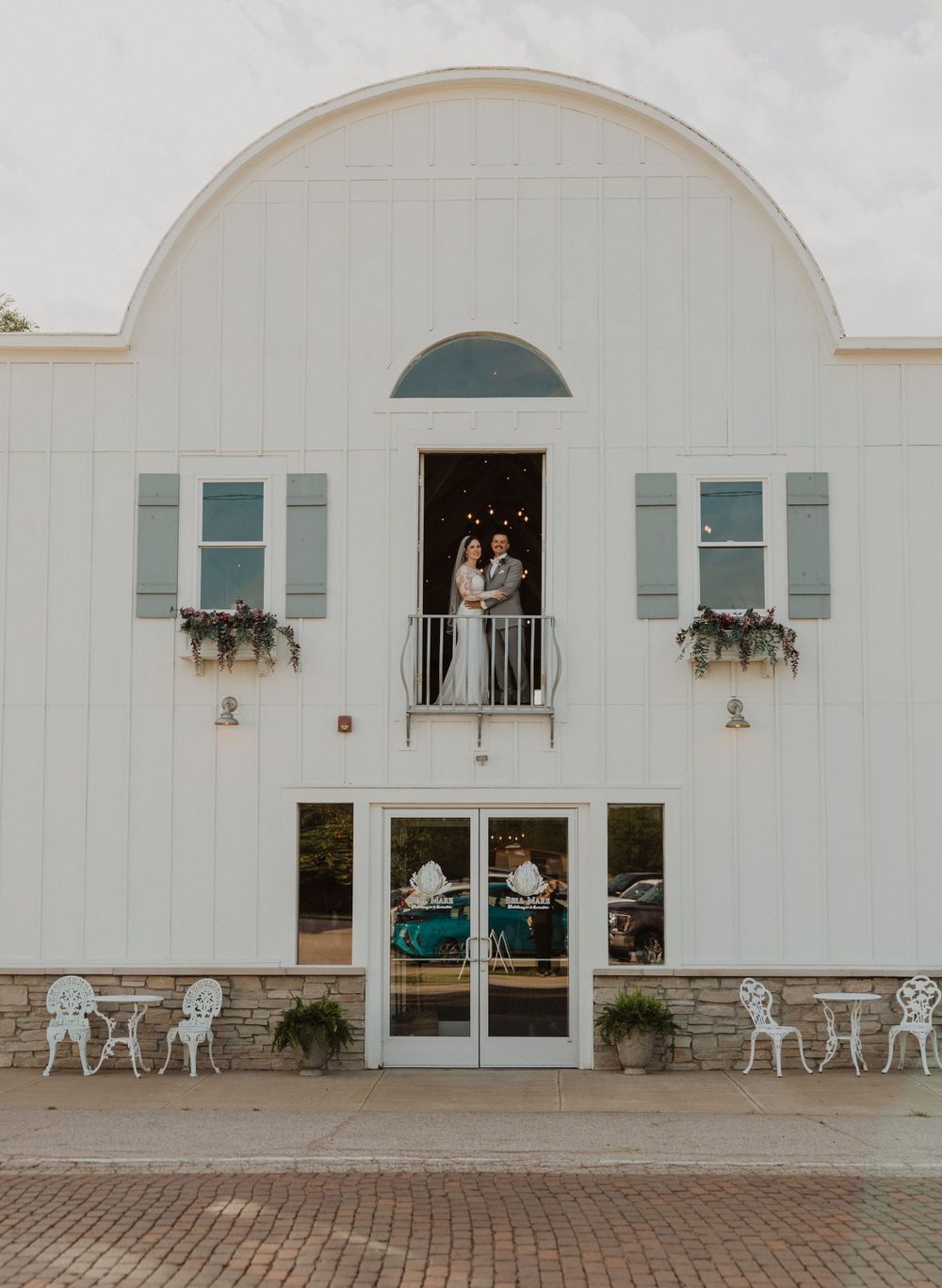 White event venue with decorative shutters and outdoor seating area on brick paved patio.