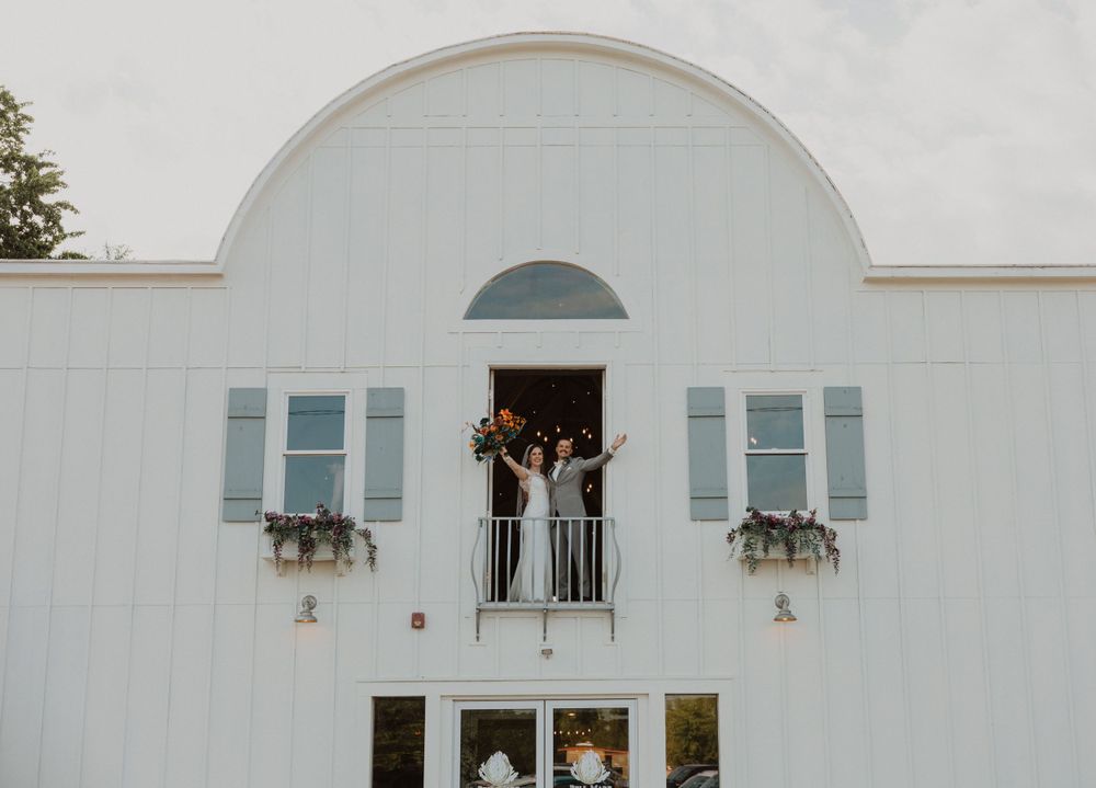 Exterior view of a white barn-style wedding venue with arched windows and decorative flower boxes.
