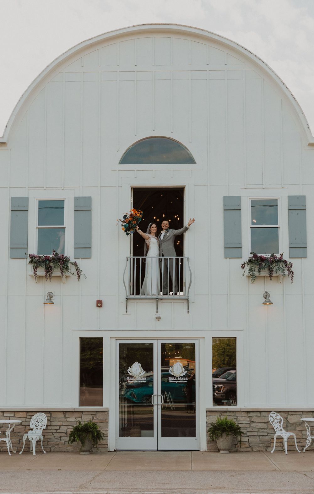 Modern white barn venue with elegant arched windows and outdoor seating areas.