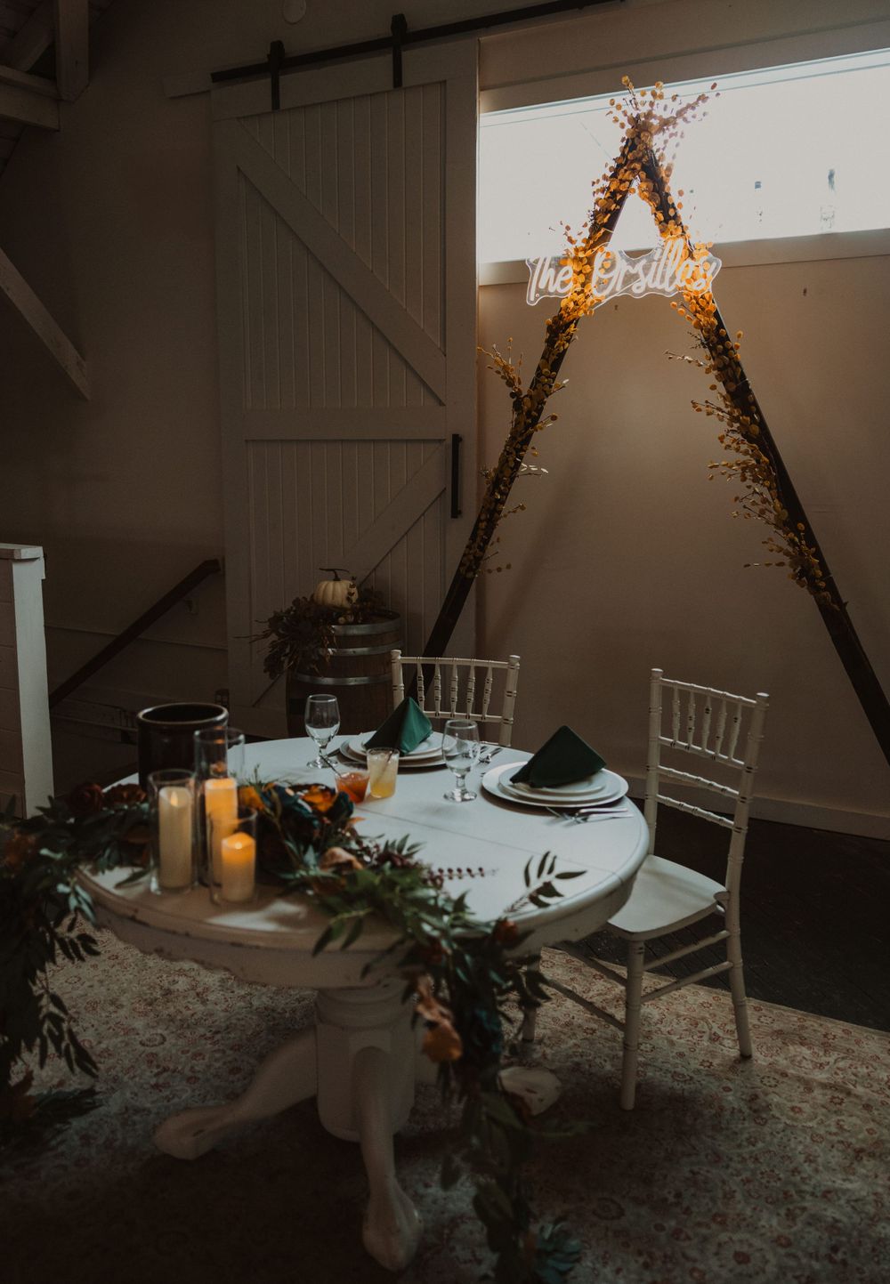 Wedding reception table setup with twinkle lights and rustic decor in a dimly lit barn venue.