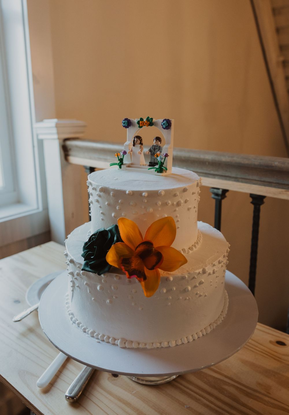 Two-tiered white wedding cake decorated with orange and navy blue floral accents.