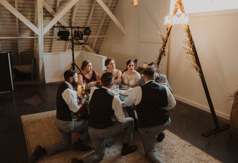 Wedding celebration in progress inside a rustic barn venue with wooden beams and warm lighting.