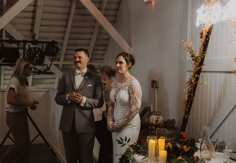 Wedding reception gathering in a barn venue with string lights and rustic wooden details.