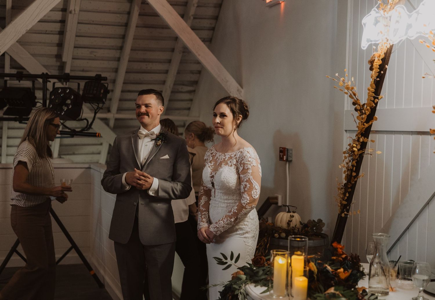 Wedding reception gathering in a barn venue with string lights and rustic wooden details.