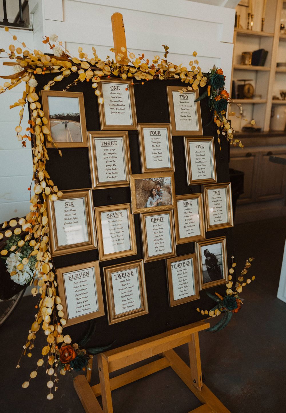 Wedding seating chart display with gold frames and floral decorations on wooden easel.