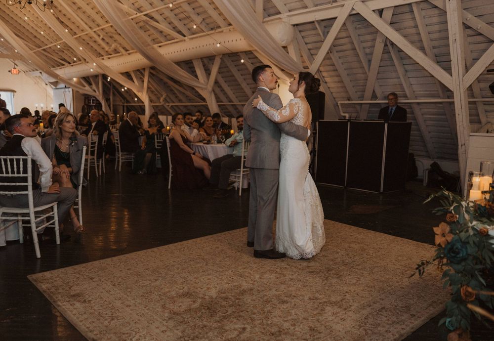 A romantic dance scene unfolds in a rustic barn wedding venue with exposed wooden beams.