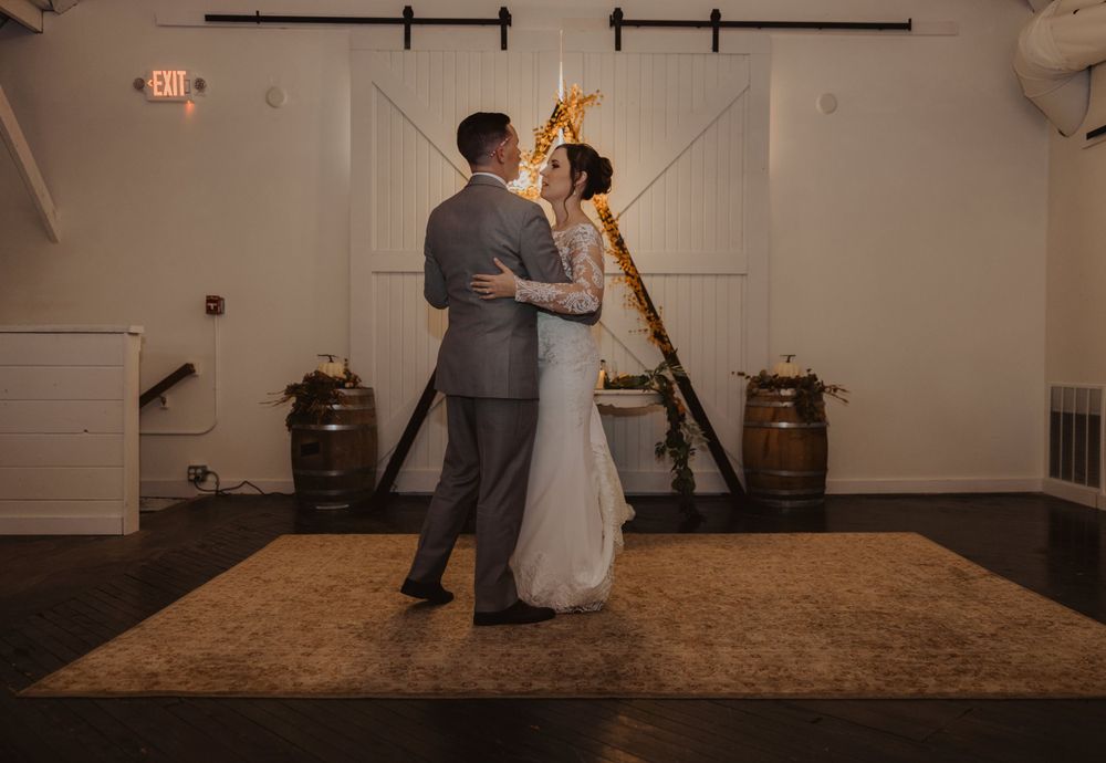 Dancers share an intimate moment on the wooden dance floor of a barn wedding venue.