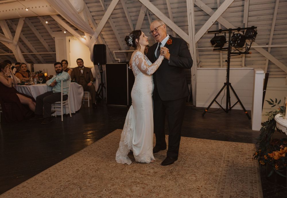 Wedding guests enjoying a dance in a warmly lit barn reception space.