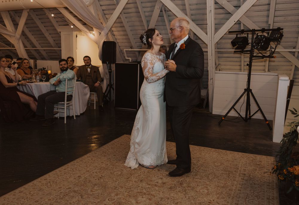 Wedding celebration with dancing couples under string lights in a rustic barn setting.
