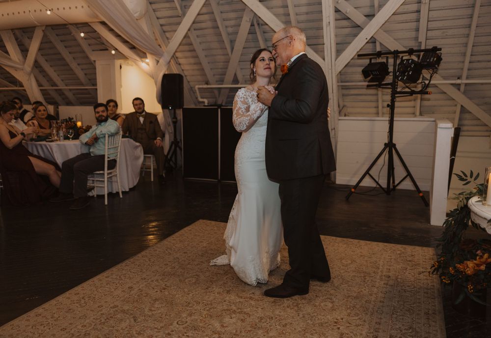 Romantic dance moment at a rustic barn wedding reception with wooden beam architecture.