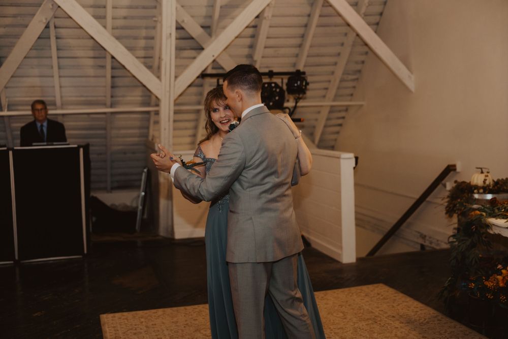 Wedding dance floor moment in a barn venue with exposed beams and ambient lighting.