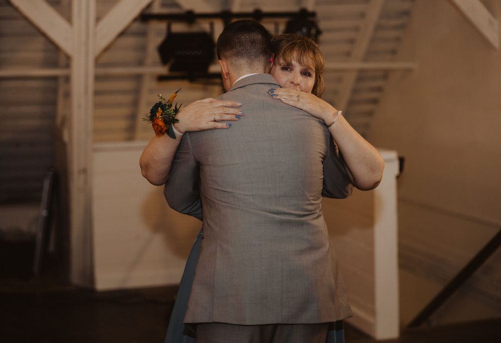 Wedding guests dance together during a reception in a rustic indoor venue with wooden beams.