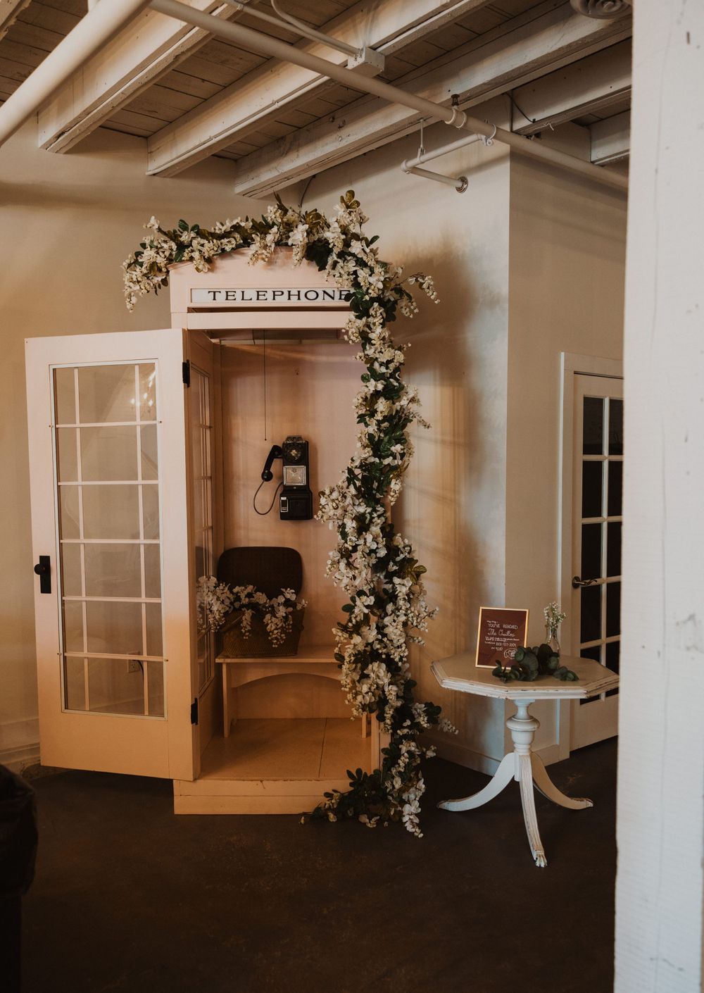 Vintage telephone booth decorated with floral garlands in wedding venue.