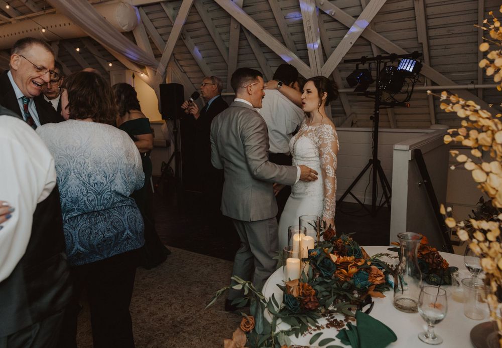 Wedding reception venue decorated with string lights and wooden beams features dancing couples.