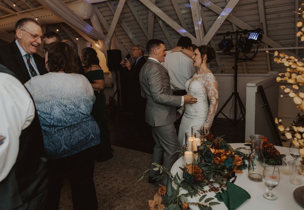 Wedding reception guests dancing and celebrating in a rustic barn venue with string lights overhead.