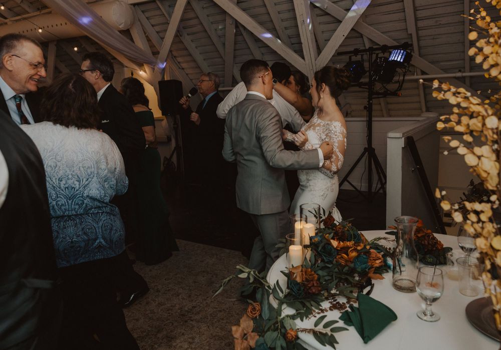 Wedding party dancing and mingling in a barn venue decorated with warm lighting and rustic decor.