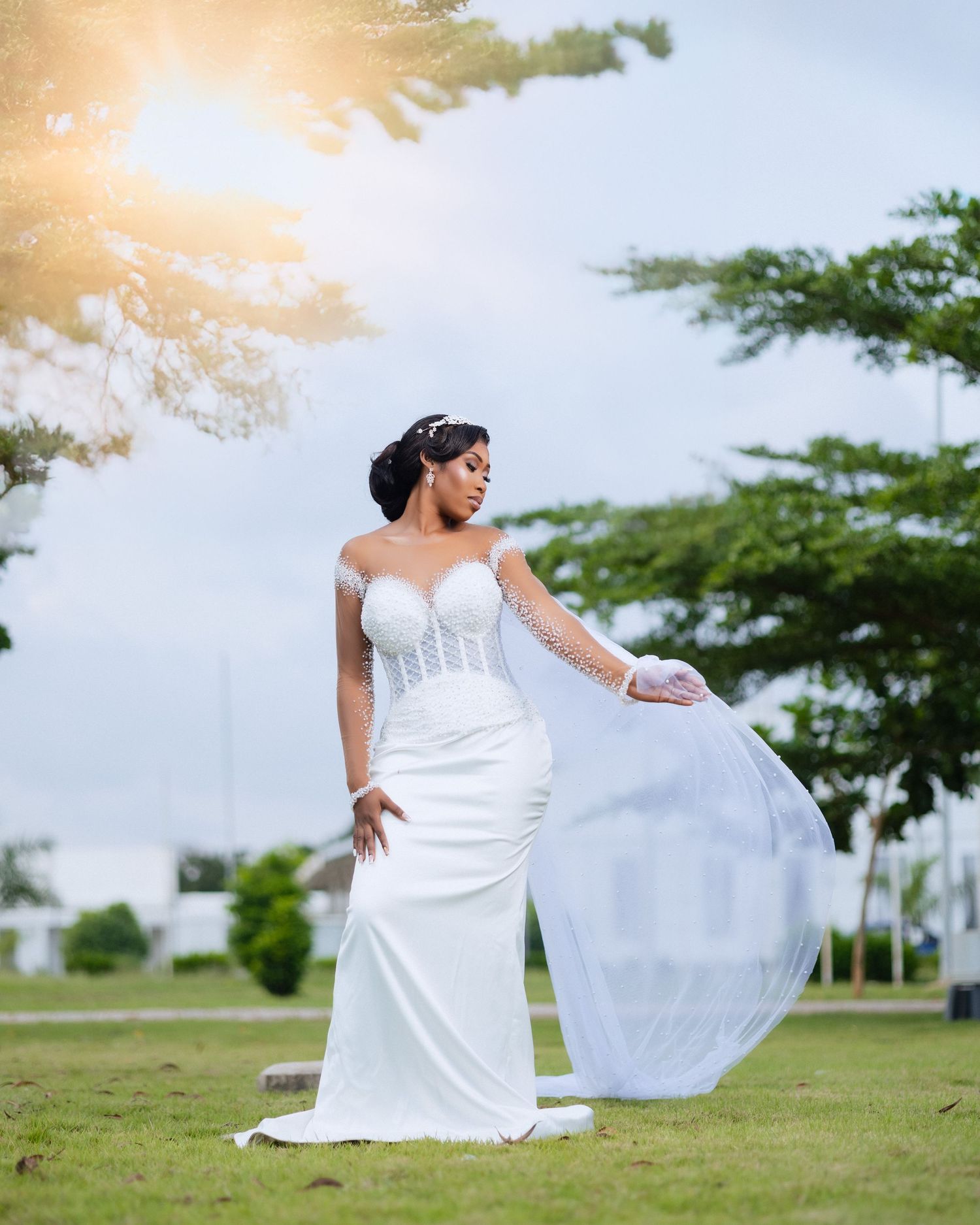 A person in a flowing white wedding dress poses gracefully on a grassy field during a sunny outdoor photoshoot.