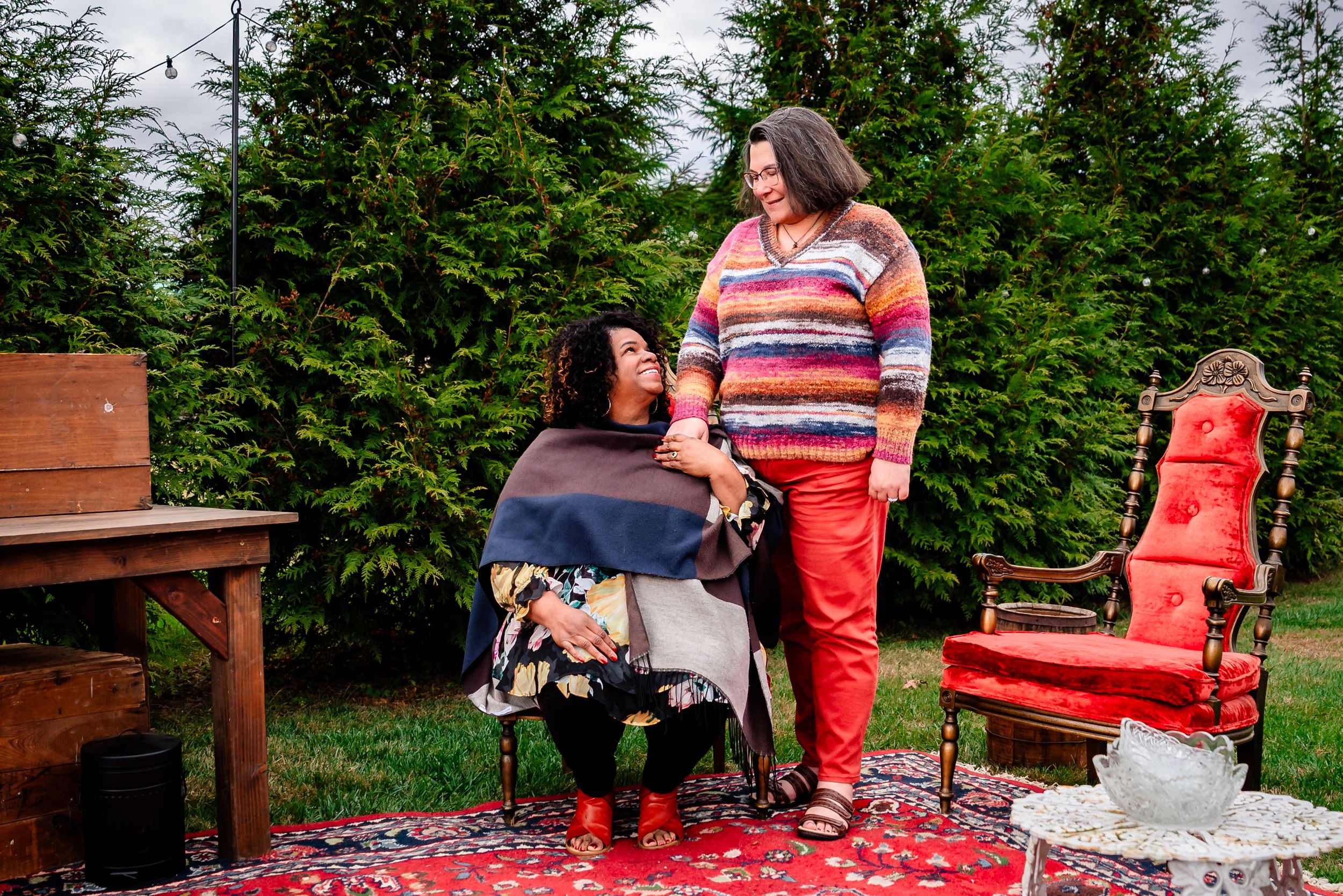 People enjoying a picnic outdoors on a red and white checkered blanket surrounded by green trees and nature.