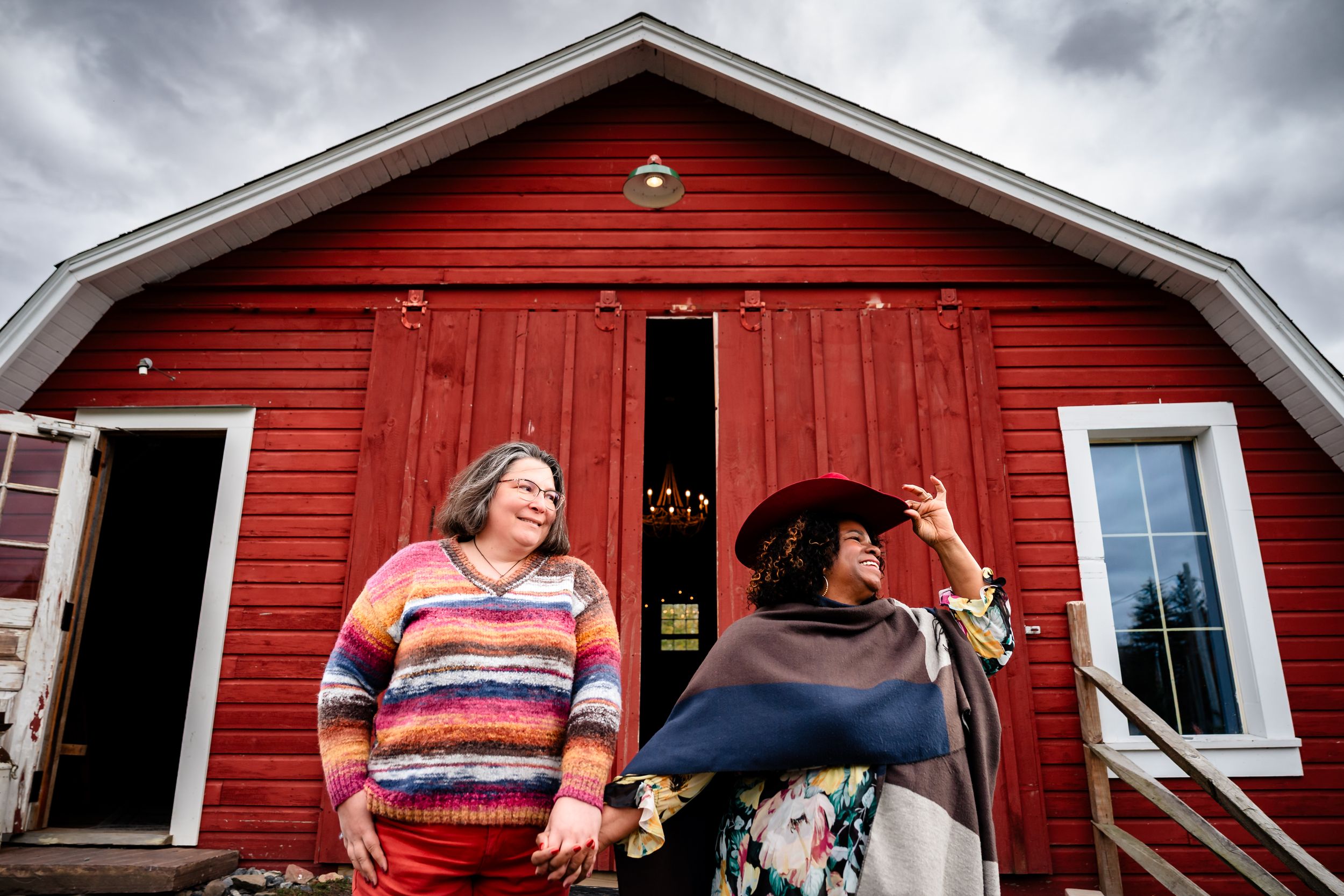 People gather outside a red barn during an outdoor celebration on a cloudy day.